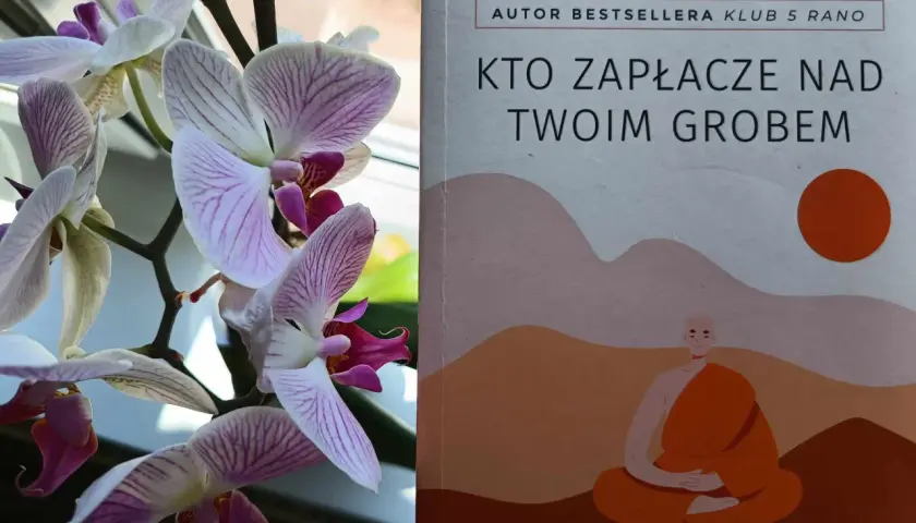 Delikatne storczyki obok książki "Kto zapłacze nad twoim grobem" Robina Sharmy, autora bestsellerów.