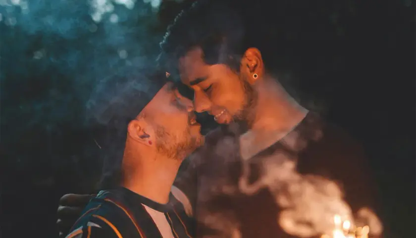 Coppia gay che si bacia con scintille e fumo, un momento intimo e passionale.