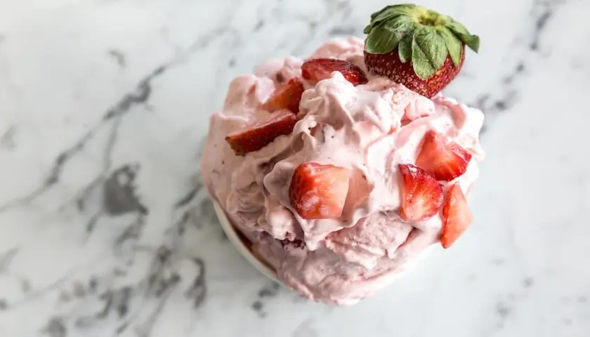 Un délice rose et crémeux : un sorbet fraise garni de morceaux de fruits frais et d'une fraise entière sur un fond marbré.