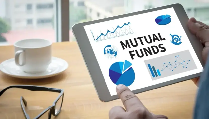 Tablet zeigt "Mutual Funds" mit Diagrammen. Ein Finger tippt auf den Bildschirm, während eine Kaffeetasse und Brille daneben liegen. Der **Ausgabeaufschlag Fonds** wird analysiert.