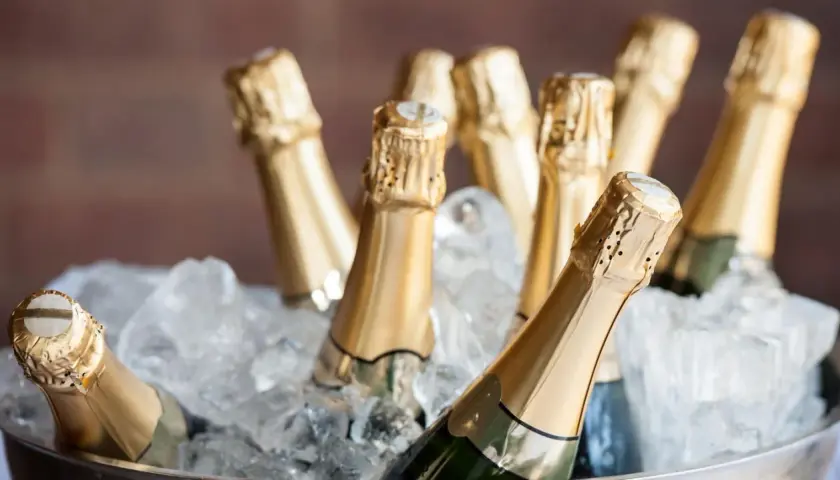 Mehrere Champagnerflaschen in goldenen Kapseln kühlen in einem Eisbad. Perfekt, um zu lernen, wie man Champagner trinkt.