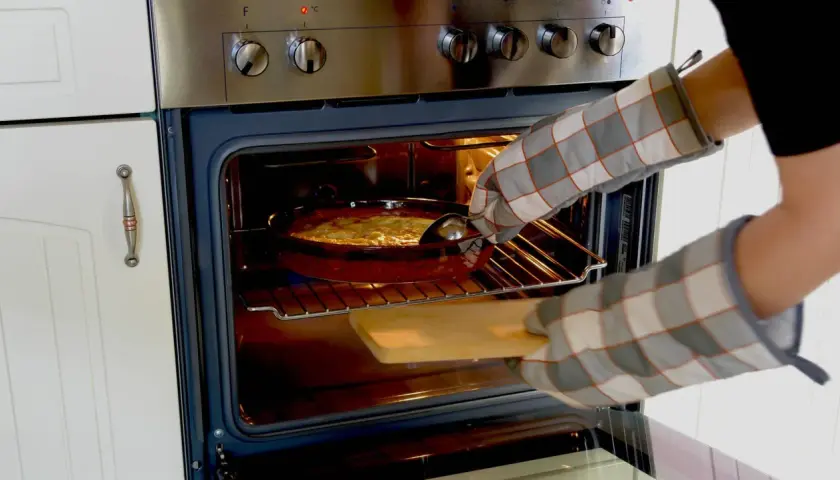Mit Ofenhandschuhen wird ein Auflauf aus dem Backofen mit Umluft genommen.