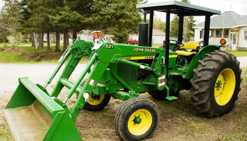 Zielony traktor John Deere 2130 z ładowaczem czołowym stoi na podwórku, gotowy do pracy.