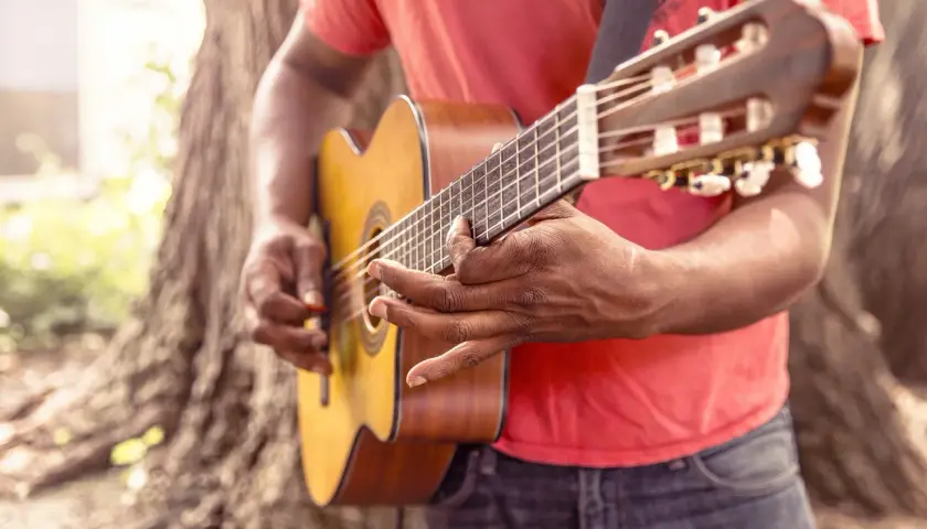 Uomo suona chitarra acustica all'aperto, ideale per imparare canzoni in inglese con testo facile.