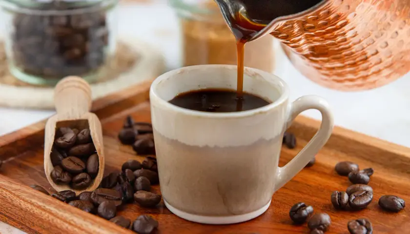 Frisch aufgebrühter türkischer Mokka fließt in eine Tasse. Kaffeebohnen liegen auf einem Holztablett.