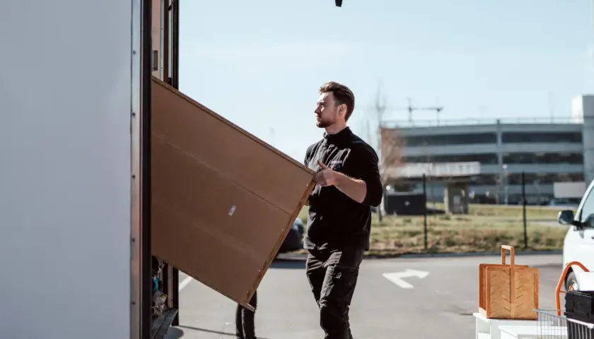 Man packar tavlor för flytt. Han bär en stor, platt kartong mot en lastbil.