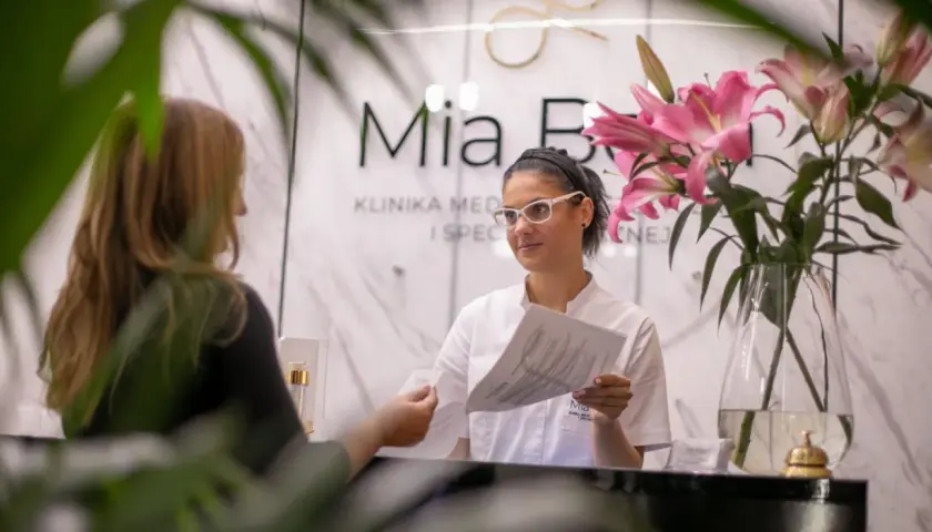 Recepcjonistka w klinice dermatologicznej podaje dokumenty klientce.