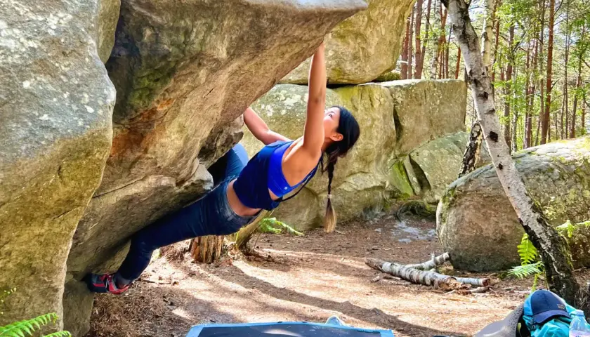 Kobieta wspina się po skale w lesie, doświadczając emocji związanych z boulderingiem w Fontainebleau.