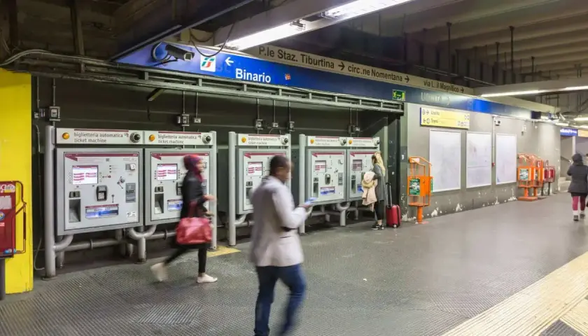 Persone acquistano biglietti alle macchinette automatiche nella stazione metro Roma EUR. Segnali indicano binari e uscite.