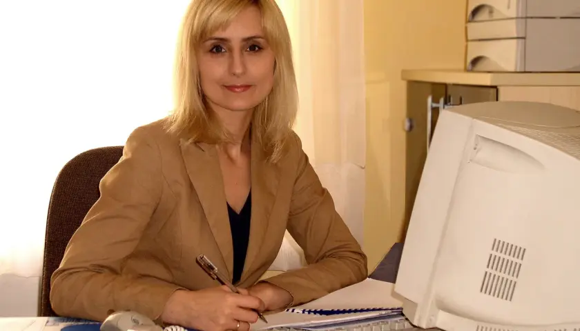 Katarzyna Matusik w lipcu pracuje przy biurku, pisząc coś na papierze. Obok niej komputer i telefon.