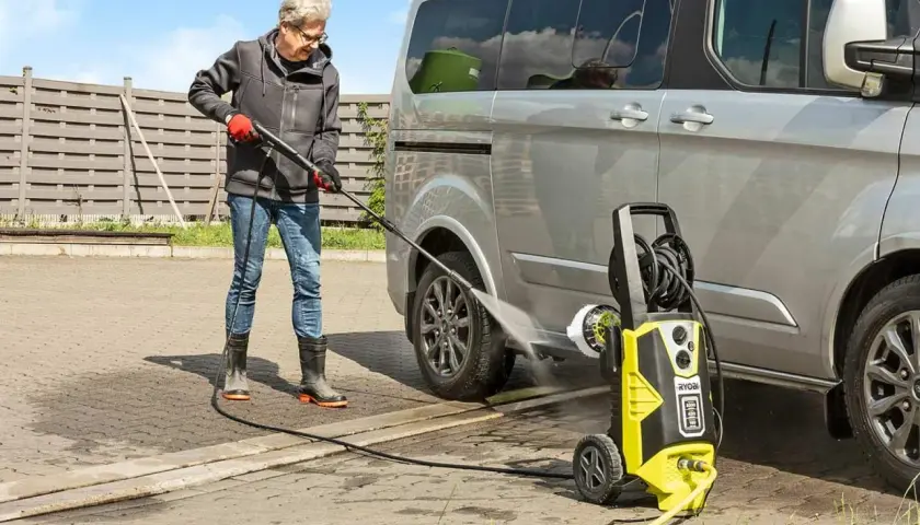 Mann reinigt Auto mit **Hochdruckreiniger**. Der **Kompressor**-ähnliche Reiniger sprüht kräftig Wasser.
