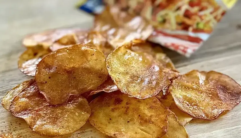 Chrupiące chipsy z piekarnika, lekko przyprawione, rozsypane na drewnianym blacie obok otwartej paczki.