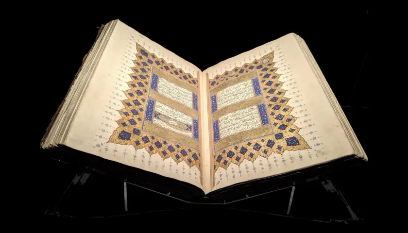 En öppen, gammal Koran på ett ställ, med detaljerad kalligrafi och gyllene ornament. En påminnelse om vem som skrev Koranen.
