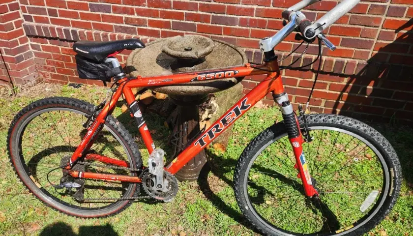 A red Trek 6500 ZX mountain bike rests on grass in front of a brick wall.