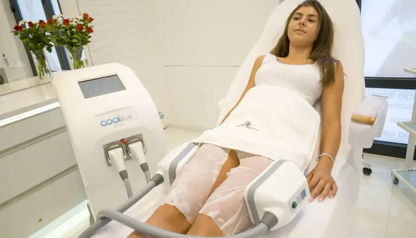 Kriolipoliza uda: dwie przyłożenia na udach kobiety leżącej na kozetce, obok urządzenia Cooltech.