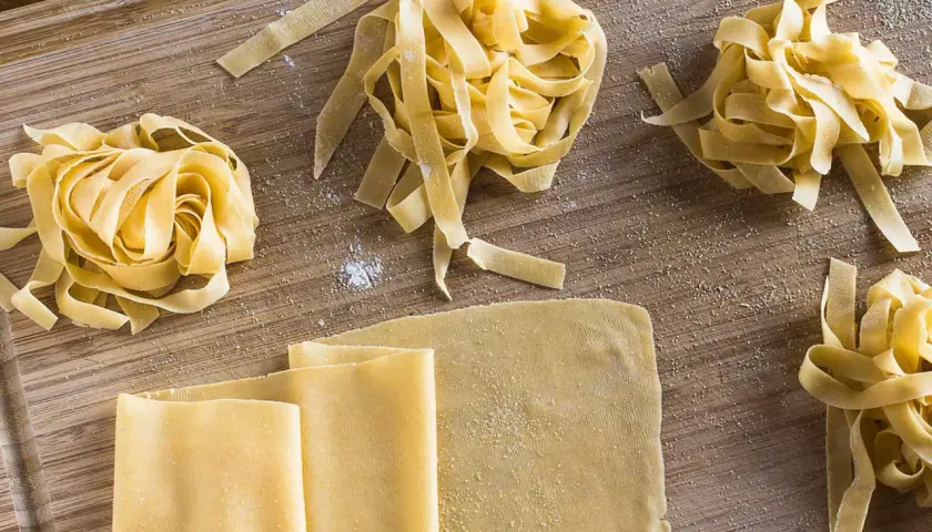 Frischer, selbstgemachter Pastateig, wie im original italienischen Rezept, liegt auf einem Holzbrett. Tagliatelle-Nester und Teigplatten warten auf ihre Zubereitung.