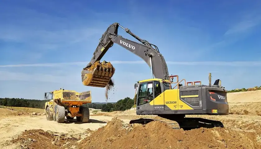 Koparka Volvo wysypuje ziemię do wywrotki. Prace ziemne, ułożenie rur w wykopie cennik bez materiału.