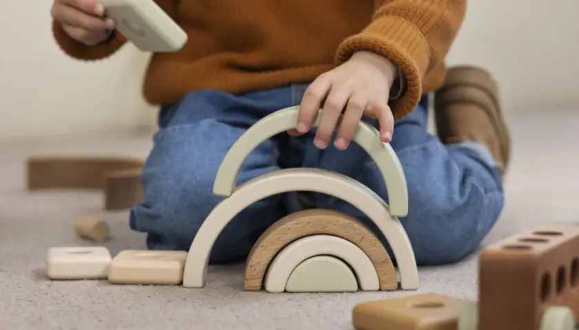 Niño jugando con bloques de madera, creando un arcoíris. Un ejemplo del sistema montessori para el desarrollo infantil.