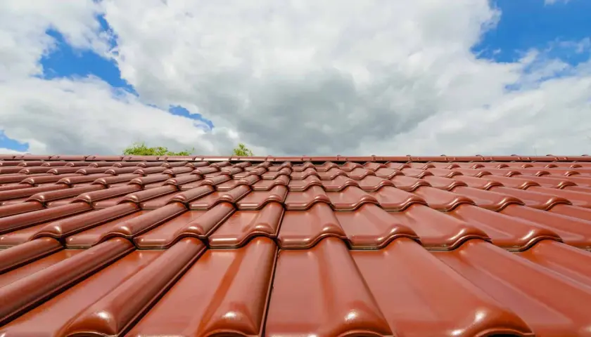 Czerwona dachówka ceramiczna lśni w słońcu. Zastanawiasz się, jaka dachówka ceramiczna najlepsza? Ta prezentuje się okazale.