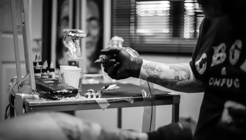 Artysta tworzy skomplikowany ornament tattoo na ręce klienta. Widać maszynkę, tusze i przygotowania do sesji.