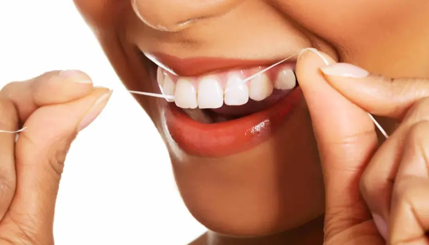 Uśmiechnięta osoba używa nić dentystyczną do czyszczenia zębów. Dbałość o higienę jamy ustnej jest ważna.