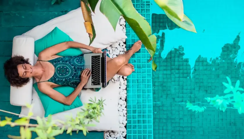 Kobieta pracująca na laptopie przy basenie. Tak żyją dzisiejsi nomadzi, kto to taki? Wolność i praca w dowolnym miejscu.