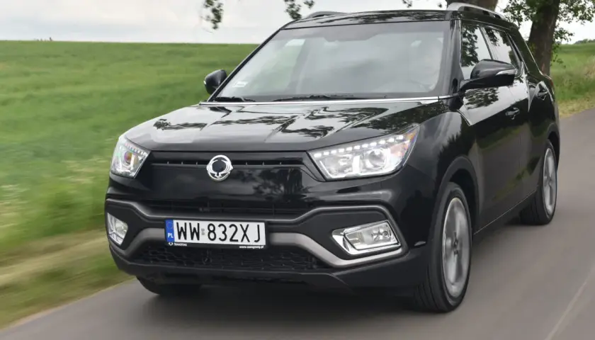 Czarny SsangYong Tivoli, model suw 2000, pędzi po wiejskiej drodze wśród zielonych pól.