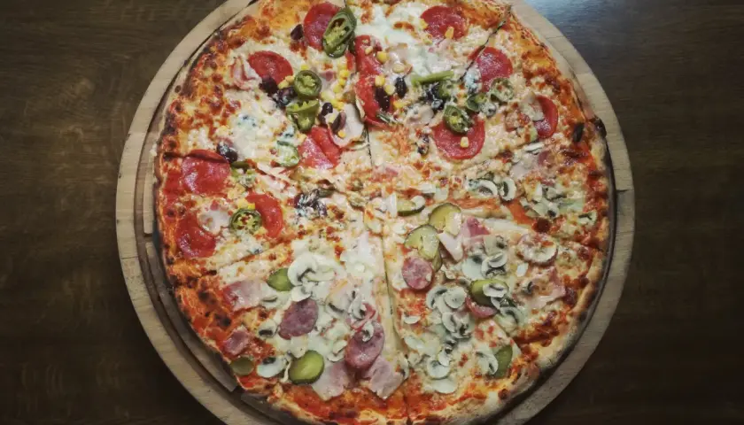 Apetyczna pizza na cienkim cieście z różnymi dodatkami: salami, pieczarki, kukurydza, papryczki jalapeno i ogórek. Zastanawiasz się, ile kalorii ma pizza na cienkim cieście?