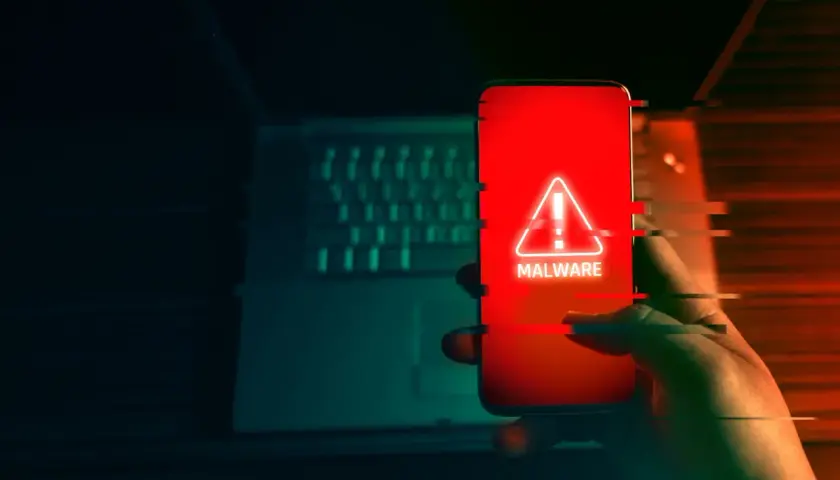 Dłoń trzyma smartfon z czerwonym ekranem i ostrzeżeniem o złośliwym oprogramowaniu. To może być początek oszustwa na blik.