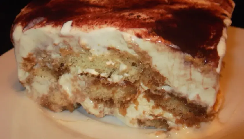 Pyszny kawałek tiramisu bez alkoholu, z warstwami biszkoptów i kremu, posypany kakao.