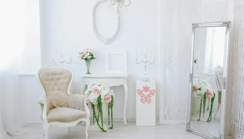 Eleganckie wnętrze w stylu shabby chic: kremowa sofa, wazon z kwiatami, lustro i świeczniki tworzą romantyczną atmosferę.