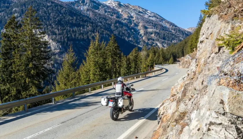 Un motociclista affronta una curva su una strada di montagna, godendosi un perfetto week end in moto tra boschi e cime innevate.