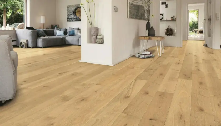 Un soggiorno moderno con parquet chiaro. Un divano grigio e un tavolino completano l'arredamento. Immagine che illustra come si monta il parquet.