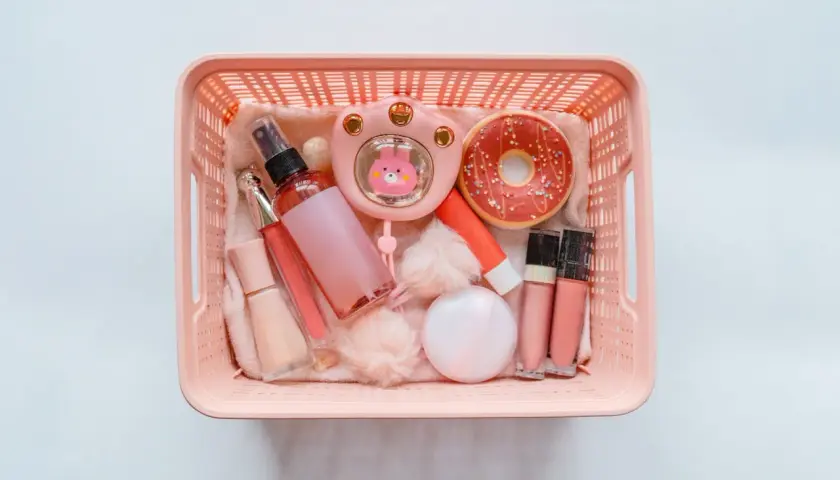Rosa korg med smink på flyget: läppglans, puder, parfymflaska och en söt liten fläkt.