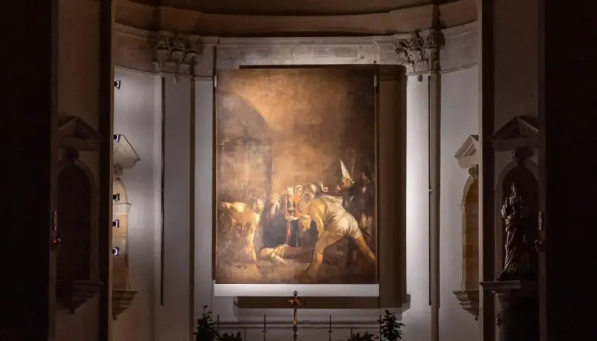 Il Seppellimento di Santa Lucia, capolavoro di Caravaggio in Sicilia, illuminato nell'oscurità di una chiesa.