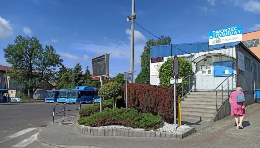 Chrzanów dworzec autobusowy. Niebieskie autobusy czekają na pasażerów, a kobieta w różowej sukience idzie w stronę budynku.