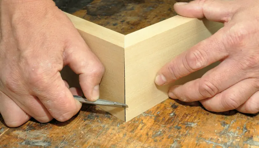 Präzises Gehrung schneiden: Hände führen ein scharfes Werkzeug an Holzleisten entlang, um eine perfekte Ecke zu schaffen. Ein kleiner Trick für saubere Verbindungen.