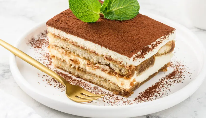 Pyszny kawałek tiramisu z mascarpone, posypany kakao i udekorowany miętą. Idealny na deser, gdy szukasz sprawdzonego przepisu.