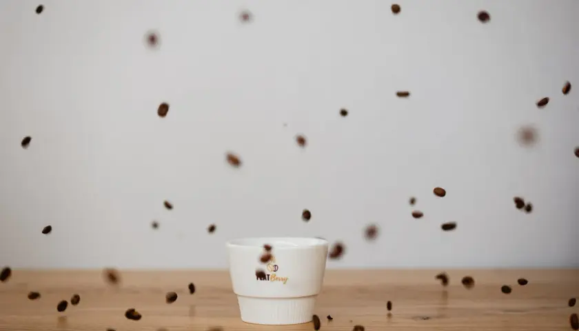 Kaffeebohnen tanzen um eine weiße Tasse. Der Duft verspricht vollen Kaffee Geschmack.