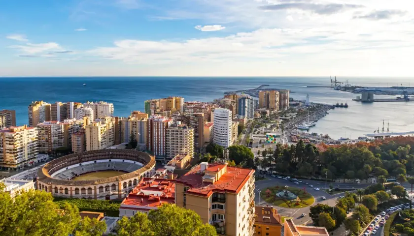 Malaga, listopad: słoneczna pogoda nad miastem, morzem i portem. Widoczna arena, budynki mieszkalne i park.