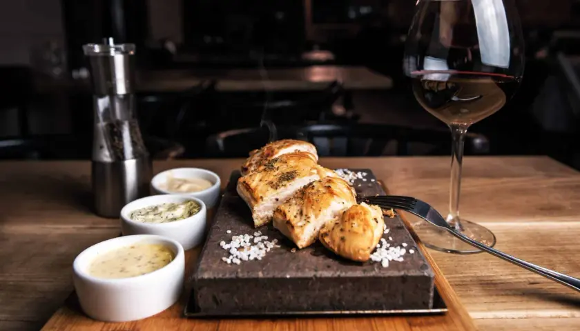Un plat de poulet grillé avec trois sauces, du sel, un moulin à poivre et un verre de vin rouge. La question est : quel vin avec viande blanche ?