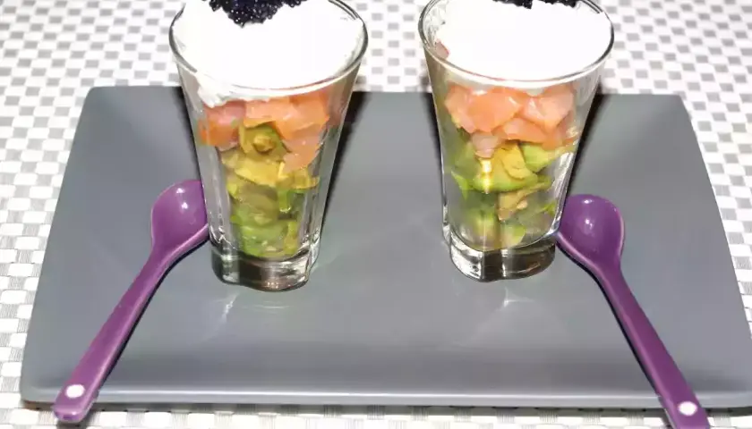 Deux verrines avocat saumon, garnies de crème et de caviar, prêtes à être dégustées avec leurs cuillères violettes.