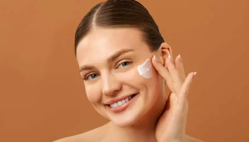 Mujer sonriente aplicándose crema facial. Una rutina de belleza con retinol y vitamina c para una piel radiante.