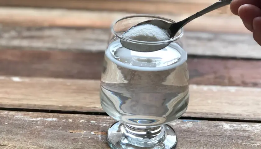 Łyżeczka z proszkiem, który może być naturalny kolagen na stawy, wsypywana do szklanki z wodą.