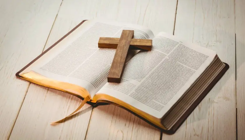 Otwarta Biblia z drewnianym krzyżem na stronach. Znajdź motywujące cytaty biblijne, które dodadzą Ci sił i nadziei.