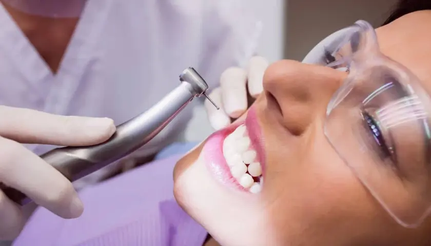 Visita dentistica per rimuovere il tartaro dai denti. La paziente indossa occhiali protettivi mentre il dentista usa uno strumento rotante.