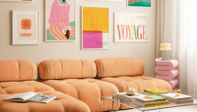Ein orangefarbenes Sofa mit bunten Bildern an der Wand. Welche Farbe passt zu Orange? Pink und Gelb harmonieren hier perfekt.