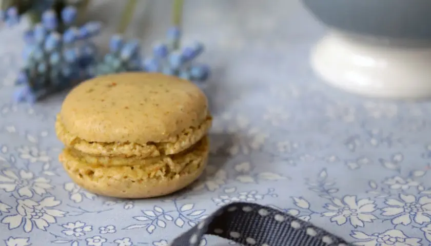Delikatne makaroniki na bezie włoskiej, w pastelowym kolorze, leżą na błękitnej tkaninie w kwiaty.