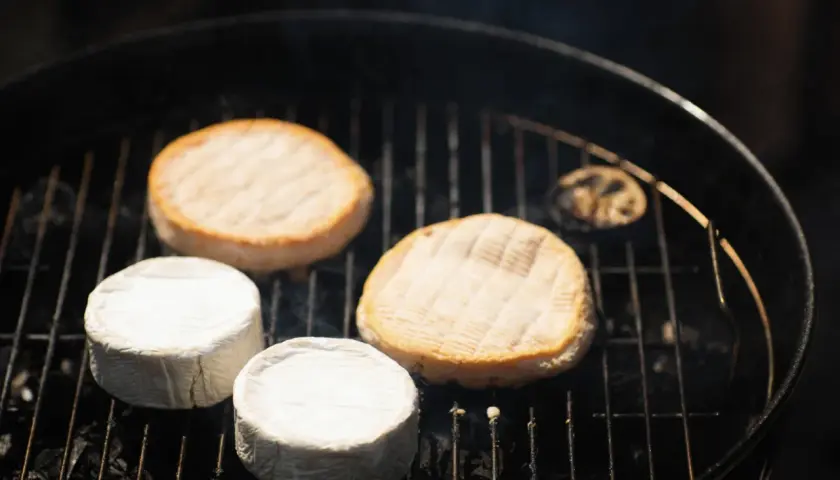 Fromages ronds, dont certains enrobés de blanc, chauffent sur un barbecue. Une idée gourmande pour un barbecue feta.