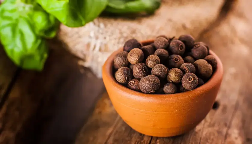 Miseczka pełna ziaren ziela angielskiego, jednego z aromatycznych spices po polsku, na drewnianym blacie.